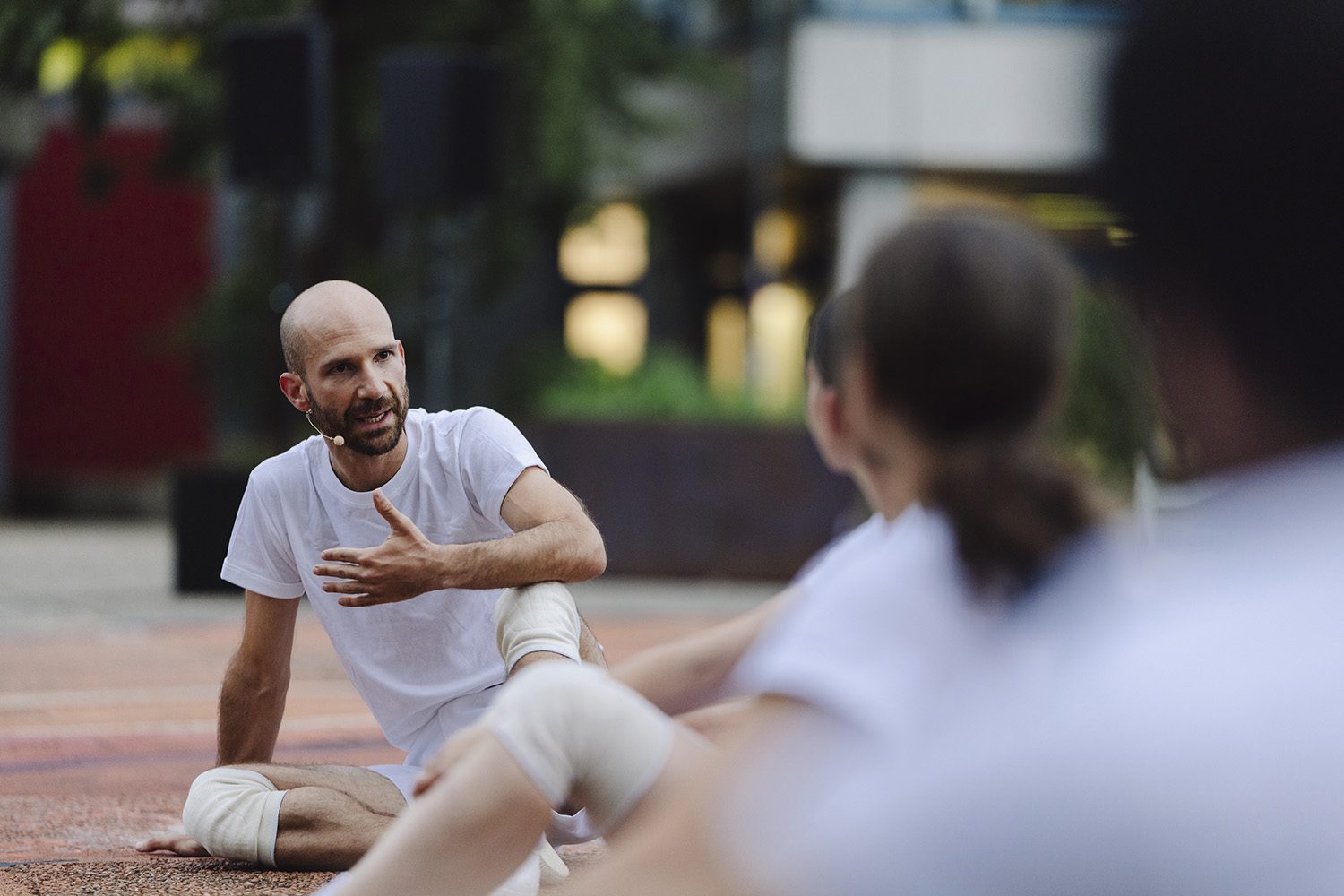 Tal sitting on the ground outdoors, talking with a group of dancers